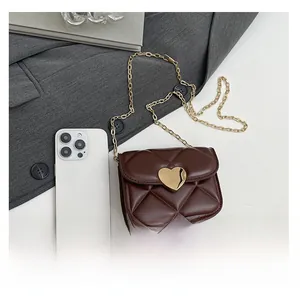 Mini sac matelassé marron avec boucle cœur dorée à côté d'un smartphone pour référence
