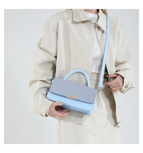 Détail d'un sac à main bleu clair avec rabat texturé tissé et finition en cuir lisse