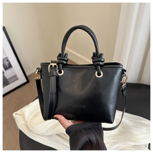 Detail of black matte leather bucket bag with gold hardware and woven knot handle
