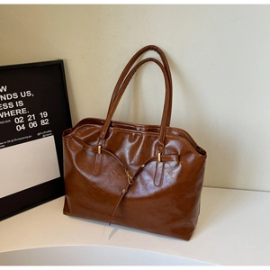 Detailed view of dark brown glossy leather tote bag with elegant metal buckle closure