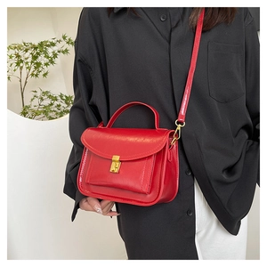Detail of red leather crossbody bag with golden metal buckle and top handle feature