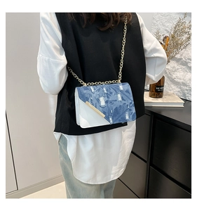 Dettaglio di borsa a tracolla in denim e pelle bianca con catena d'oro e finiture in metallo