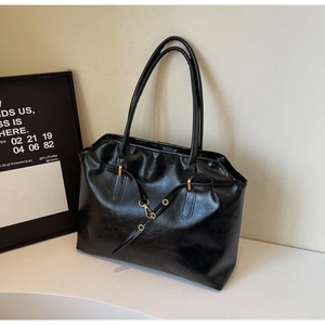 Detail of black glossy tote bag featuring gold hardware and slim cylindrical handles