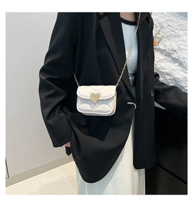 Detail of white quilted crossbody bag with golden heart-shaped twist lock on a model