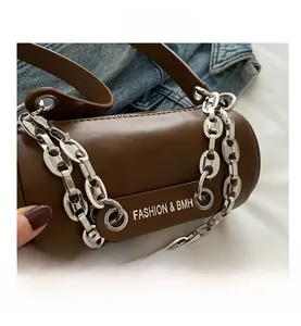 Detail of cylindrical leather bag with silver chain strap on denim background