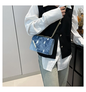 Dettaglio del patchwork in denim invecchiato e pelle sulla borsa a tracolla con catena