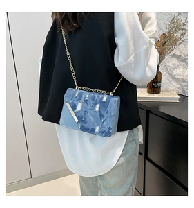 Dettaglio borsa a tracolla in denim blu con bordi sfrangiati e catena dorata sulla modella