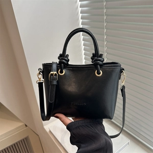 Black minimalist bucket handbag with knotted handles and gold hardware in hand-held view