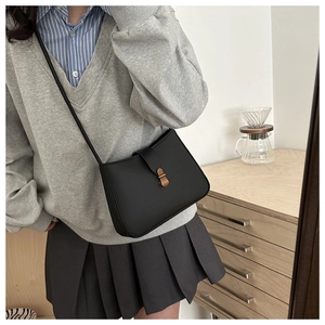 Detail of a vintage black crossbody bag with a gold oval buckle and matte leather texture