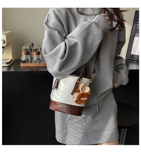 Détail du sac seau bicolore avec base en cuir marron et breloque petit monstre en peluche