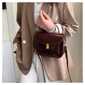 Détail du sac à bandoulière en cuir verni marron foncé avec finition brillante et fermoir doré