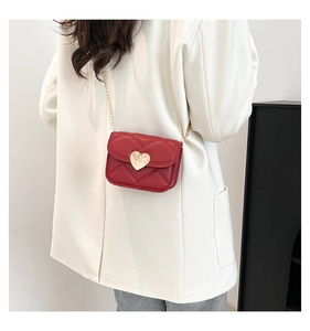 Détail du mini sac bandoulière matelassé rouge avec fermoir coeur doré sur un mannequin