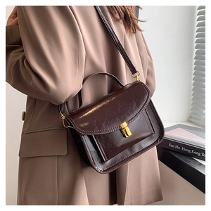 Gros plan d'un sac messager vintage en cuir marron avec fermoir doré porté par un modèle