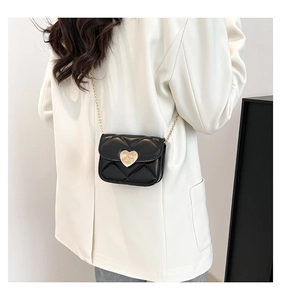 Détail du mini sac matelassé noir avec fermoir cœur porté sur un blazer blanc pur