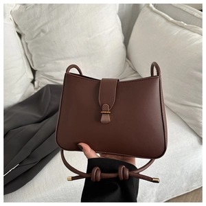 Detailed close-up of brown matte leather bag with vintage gold buckle and knotted strap