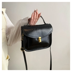 Détail d'un sac à main en cuir verni noir avec un fermoir métallique rectangulaire doré