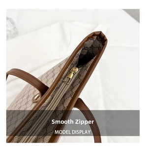 Detail shot of smooth gold-tone zipper closure on a brown textured tote bag