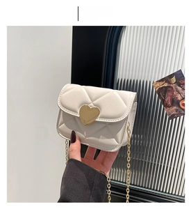Détail d'un sac à main matelassé blanc avec fermoir cœur doré et bandoulière chaîne