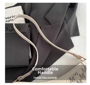 Dettaglio tracolla in pelle beige con fibbia dorata e motivo M sulla borsa a spalla