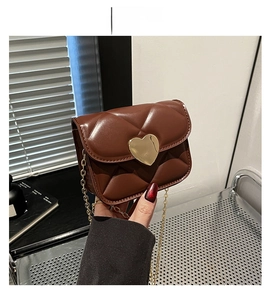 Détail d'un sac matelassé marron avec fermoir coeur doré et bandoulière en chaîne