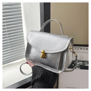 Détail d'un petit sac carré argenté avec fermoir rotatif doré et poignée supérieure