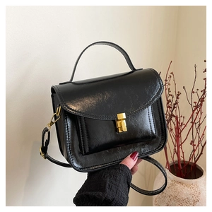 Détail d'un sac à main noir texturé avec fermoir doré sur un fond minimaliste