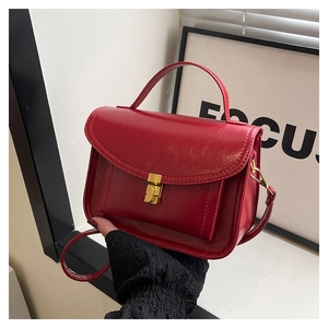 Détail d'un sac à main en cuir verni rouge avec un fermoir doré et une poignée chic