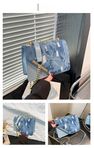 Dettaglio della borsa a tracolla in denim blu con tessuto usurato e catena dorata