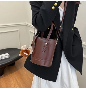 Sac seau en cuir marron foncé avec charme en peluche porté sur un blazer noir