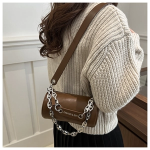 Brown leather cylinder bucket bag worn by model with wide strap and silver chain detail
