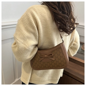 Detail of brown underarm bag with M-letter jacquard pattern and 3D bow decoration