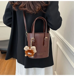 Détail d'un sac seau en cuir marron foncé avec un porte-clé peluche et une poignée