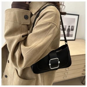 Minimalist black baguette bag with silver metal buckle styled on a wool coat