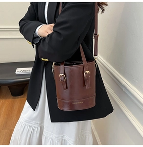 Sac seau chic en cuir marron foncé avec boucles dorées porté par un mannequin en costume