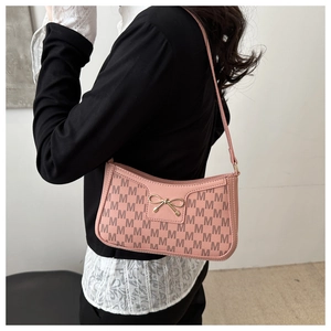 Pink underarm bag with M-monogram pattern and golden bow detail shown on a model