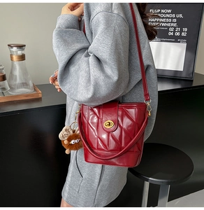 Détail du sac seau rouge matelassé avec fermoir doré et breloque ours sur un mannequin