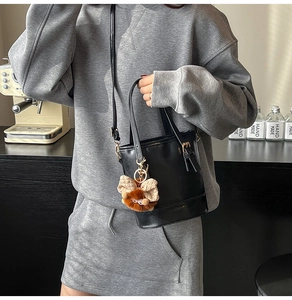 Détail d'un sac seau en cuir noir avec ferrures dorées et breloque en forme d'ours