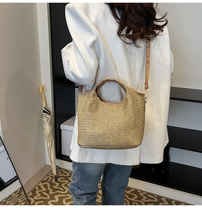 Detail of woven straw tote bag with shoulder strap worn over white blazer