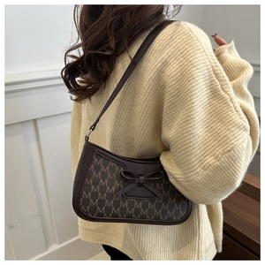Detail of dark brown baguette bag with all-over M pattern and leather bow accent