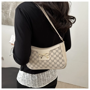Close-up of cream white underarm bag with M-pattern print and gold bow clasp detail