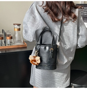 Détail d'un sac seau noir avec un pendentif nœud en peluche et une bandoulière amovible