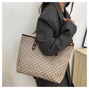 Detail of a large beige monogram tote bag with brown leather handles and gold studs