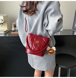 Détail d'un sac seau rouge matelassé avec fermoir doré et breloque sur mannequin