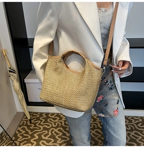 Detail of woven straw tote bag featuring brown leather trim and adjustable crossbody strap