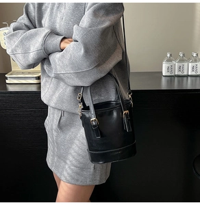Détail du sac seau noir brillant avec boucles dorées et bandoulière réglable chic