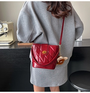 Detail of red quilted bucket bag with gold clasp and plush charm on a shoulder strap