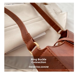 Macro shot of brown faux leather baguette bag showing golden metal ring hardware and stitching