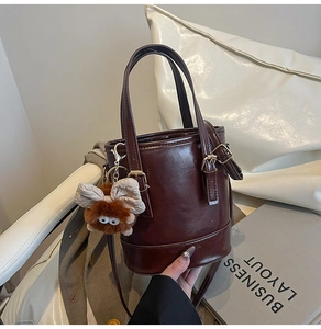 Détail d'un sac seau marron foncé en PU brillant avec un joli pendentif ours en peluche