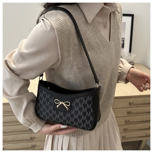 Dettaglio di una borsa a spalla in ecopelle nera con motivi M grigi e fiocco dorato