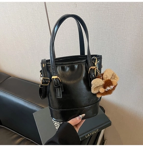 Détail du sac seau en cuir verni noir avec un pendentif en peluche et boucles dorées